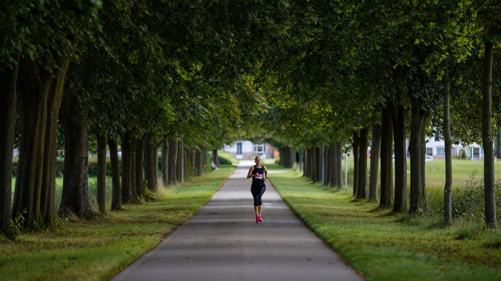 Coureuse amateur en footing facile sur un chemin arboré respirant calmement sans marque visible